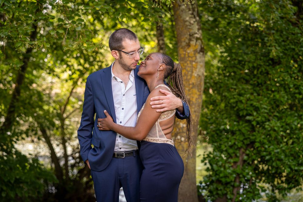 Couple shares romantic moments in a lush green garden setting during a sunny outdoor photo session.