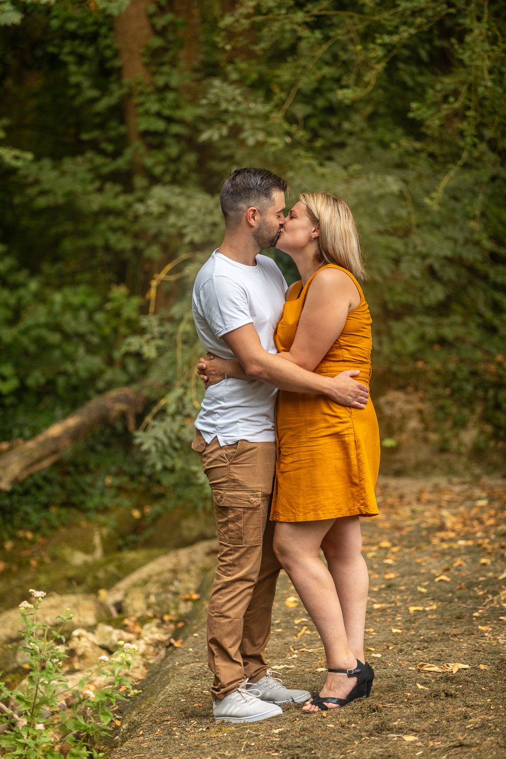 Romantic couple sharing intimate moments on a forest path covered in autumn leaves.