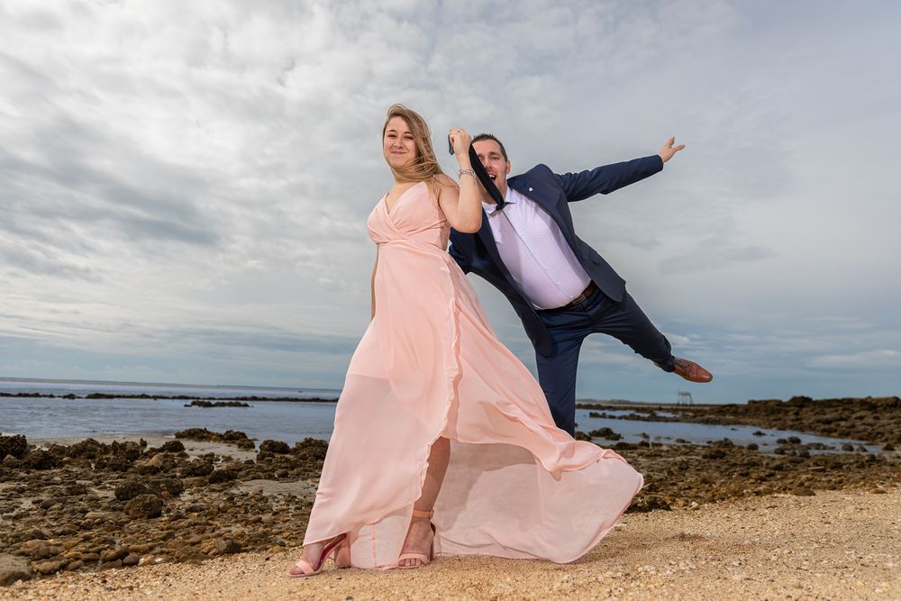 A romantic photoshoot on a scenic beach with flowing pink dress and dramatic coastal landscape.