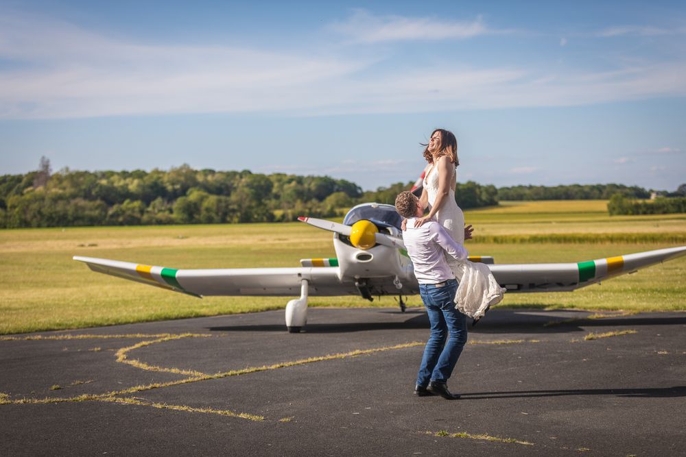 Romantic couple posing playfully with a small aircraft on an airfield runway during golden hour.