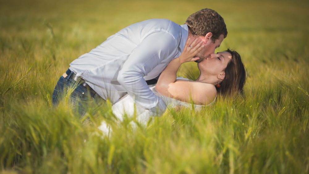 Couple laying in a golden wheat field during a romantic outdoor photo session at sunset.