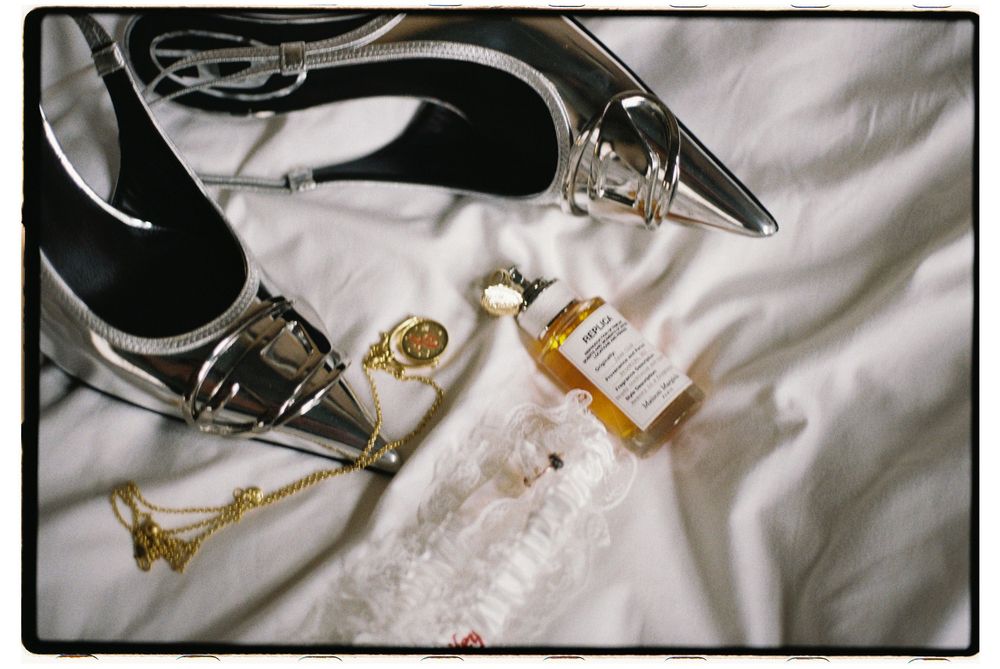 Black formal shoes with metallic accents displayed on white satin fabric next to jewelry and accessories.