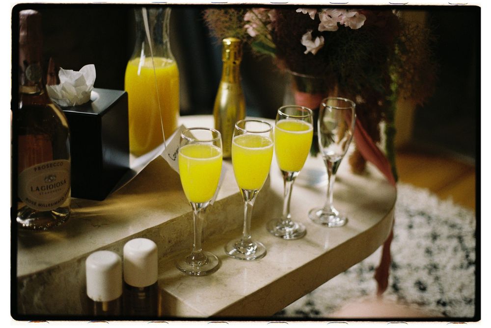 Row of champagne flutes filled with mimosas and orange juice on a wooden surface with floral decor.