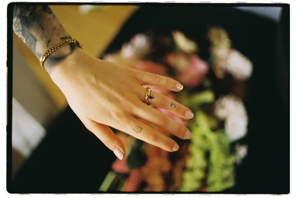 A close-up macro shot of a person's hands touching pink flower petals in a garden setting.