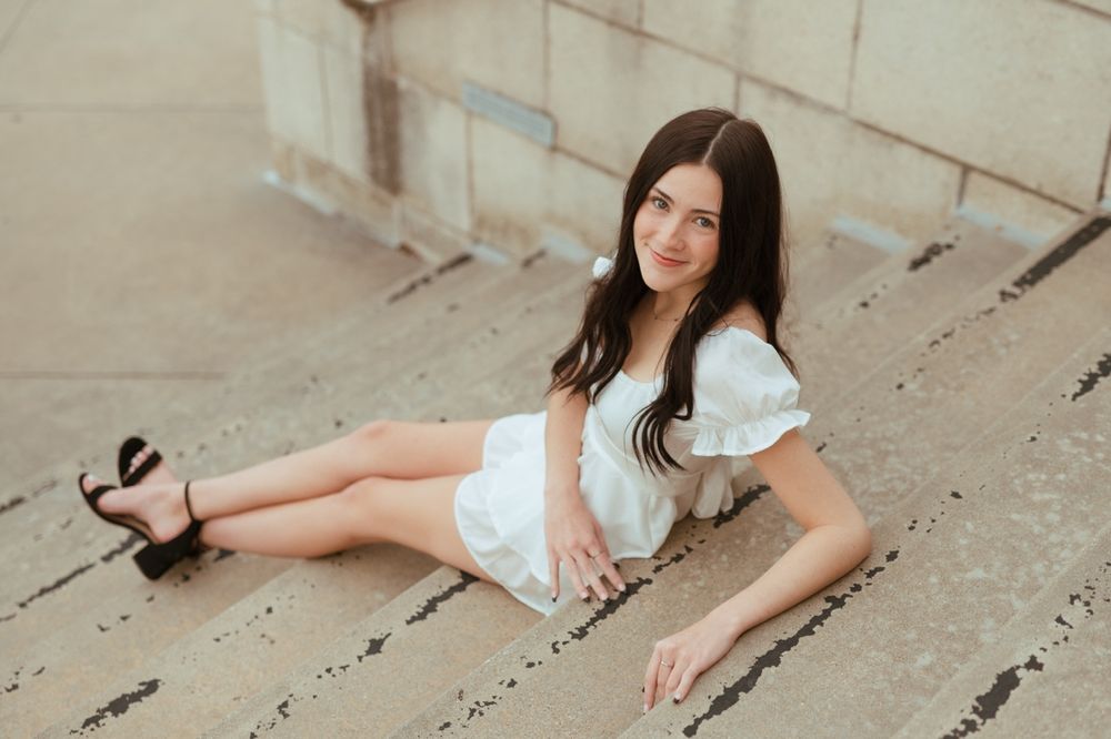 Woman in white dress and heels sitting on concrete stairs with a soft dreamy portrait style.