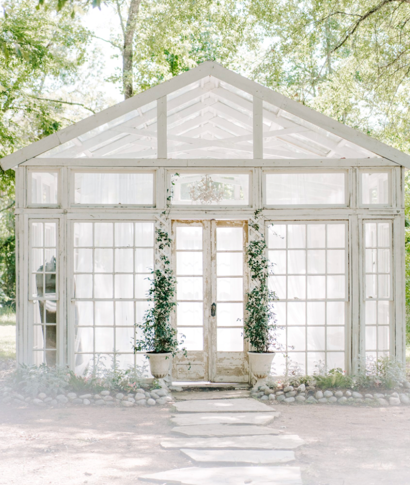 Elegant white glass-enclosed venue showcasing natural light and greenery for outdoor-indoor events with subtle column details.