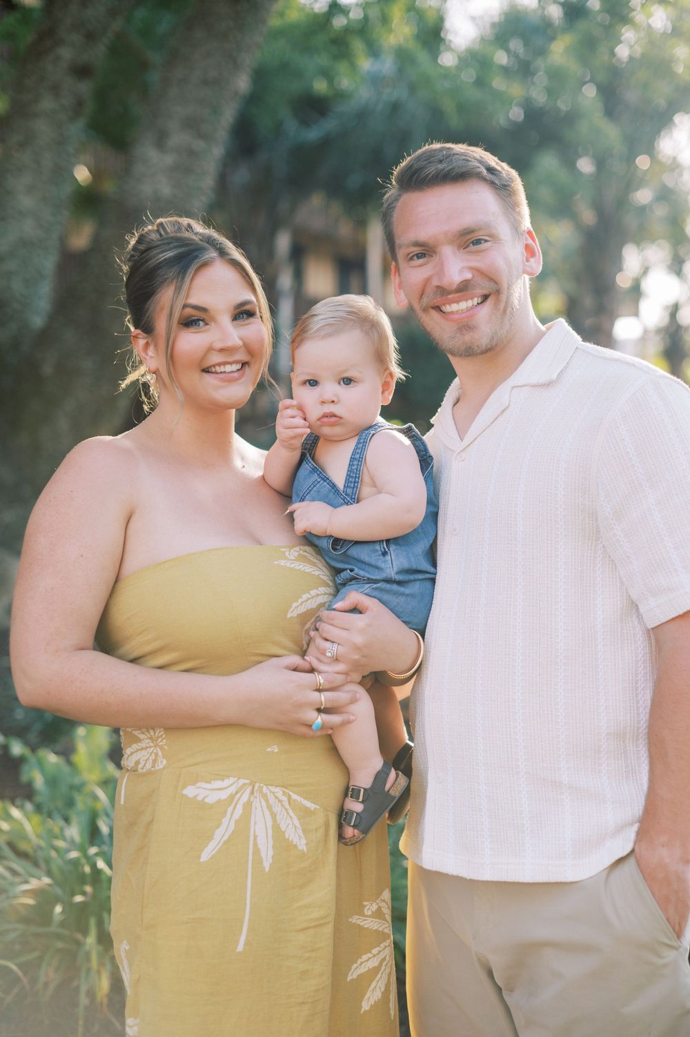 A family of three shares joyful moments together in an outdoor setting wearing yellow and white outfits.