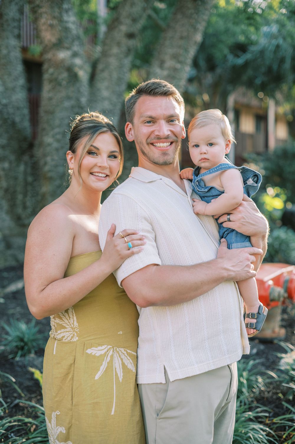 A beautiful outdoor family portrait with a baby wearing denim overalls in a lush garden setting.