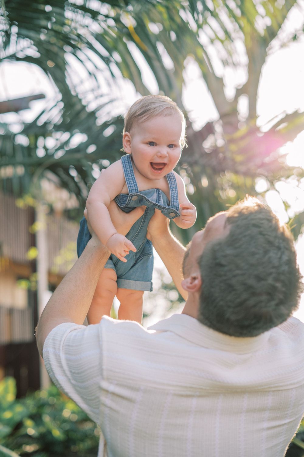Joyful moments between parent and baby against palm tree background.