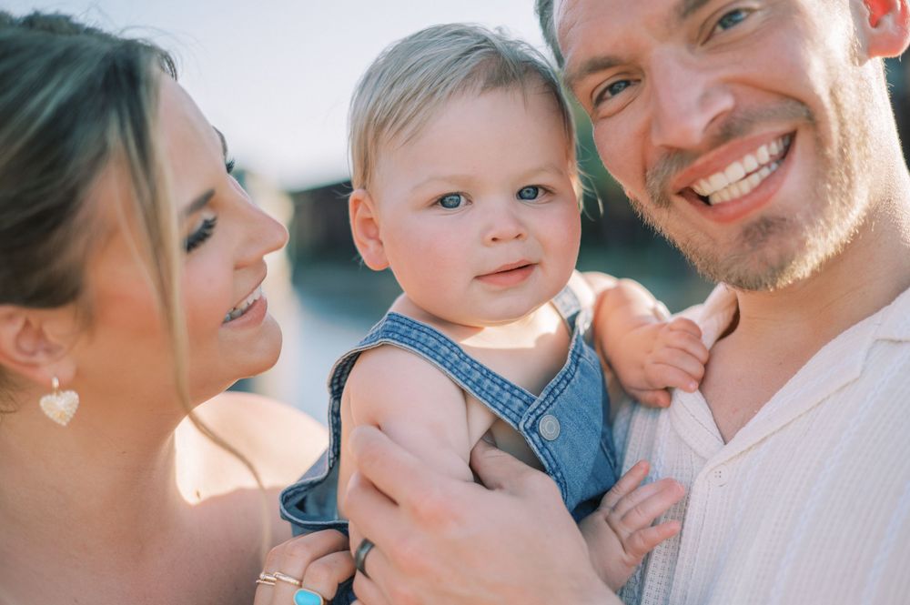 Sweet family portrait with baby in denim overalls enjoying a sunny outdoor moment together.