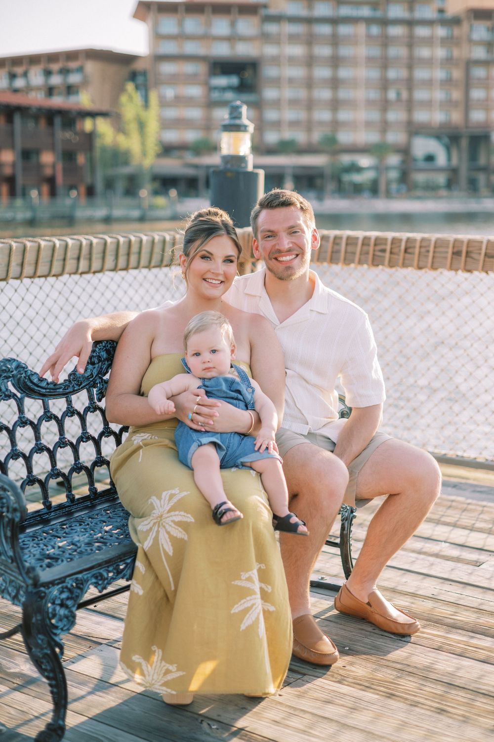 A family sitting together on a decorative bench at a waterfront boardwalk during golden hour.
