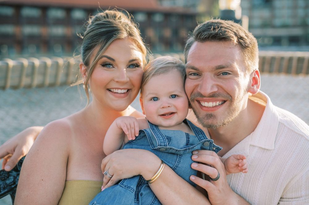 A family smiling together outdoors on a sunny day near a waterfront pier.