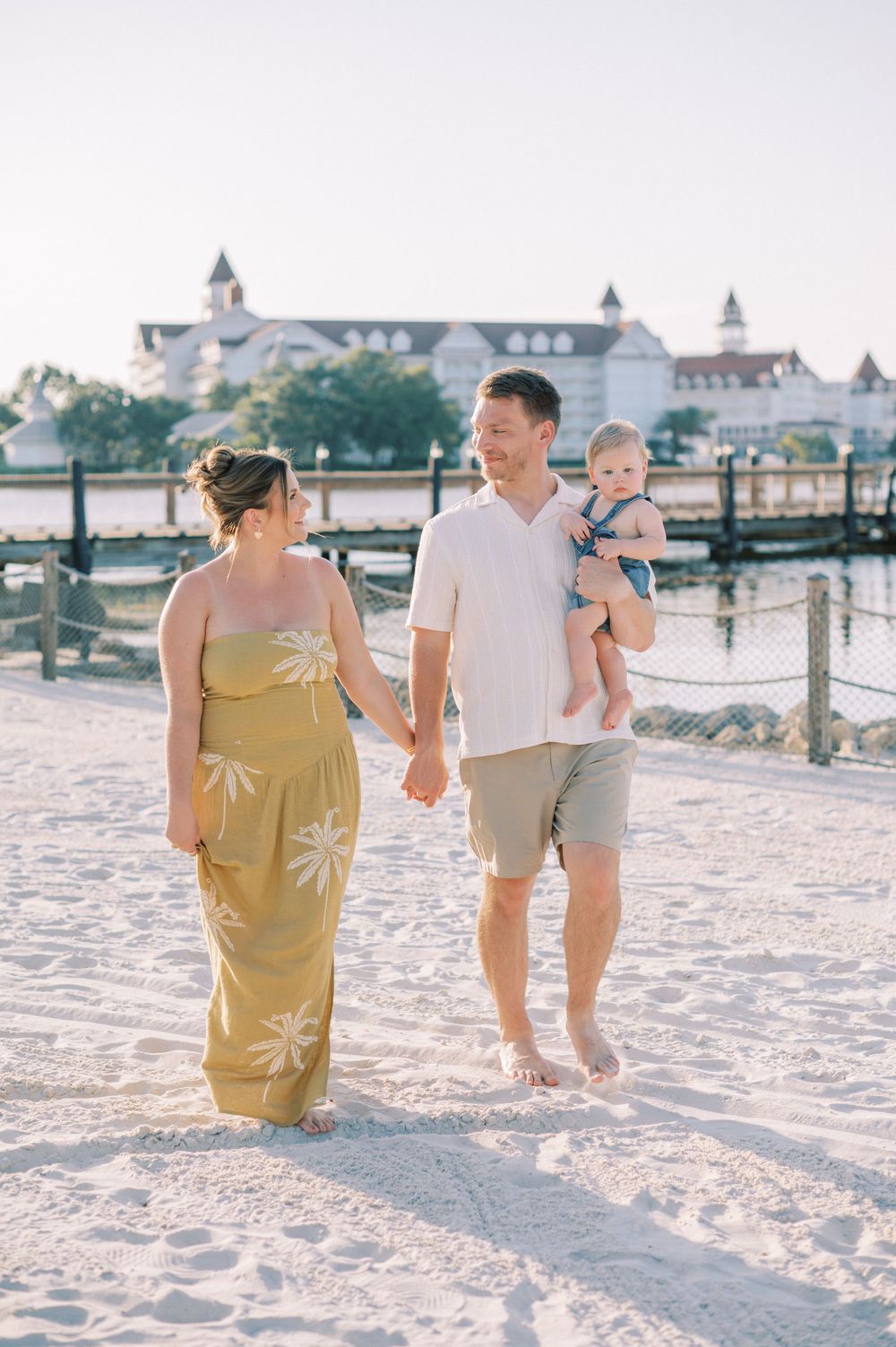 Family walking together on sandy beach with resort buildings in background.