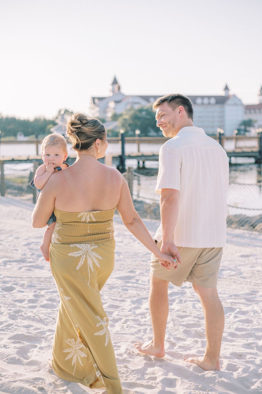 Family strolling along beach boardwalk at sunset wearing summer attire.