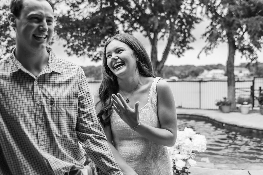 Black and white photo of a couple enjoying a light-hearted moment together by a lake, both laughing joyfully.
