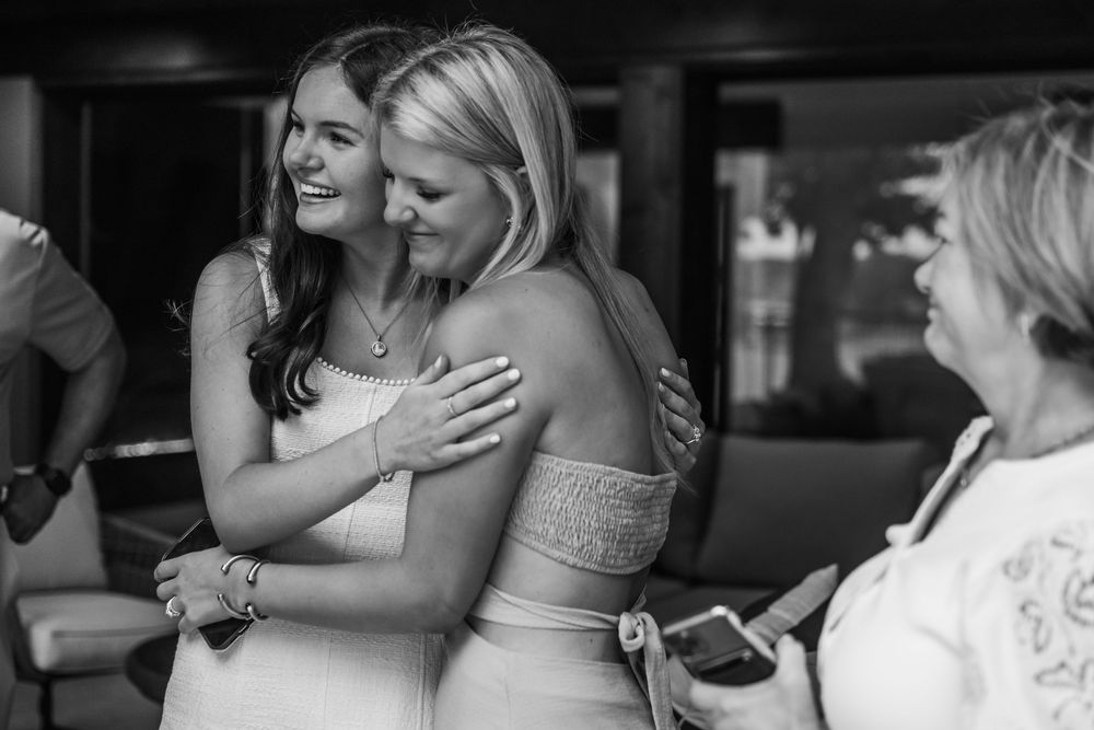 Two people share an emotional embrace at what appears to be a wedding celebration, captured in black and white photography.