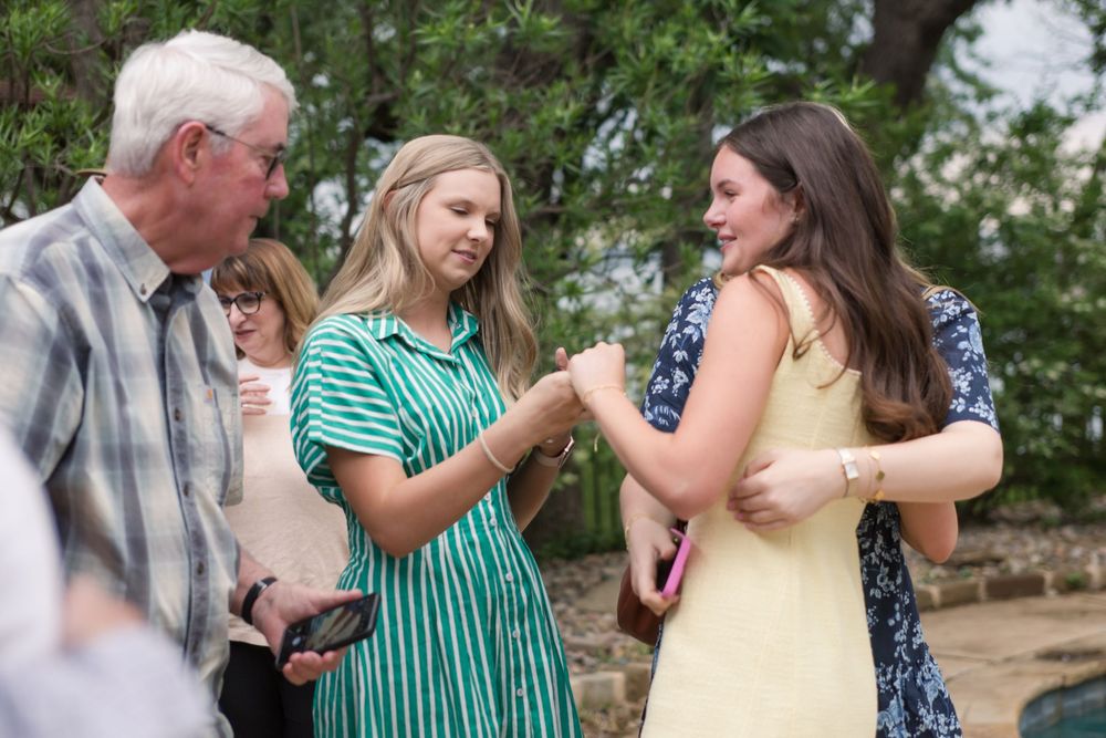 A group of people share a joyful conversation outdoors on a sunny day, with one wearing a striped green dress.