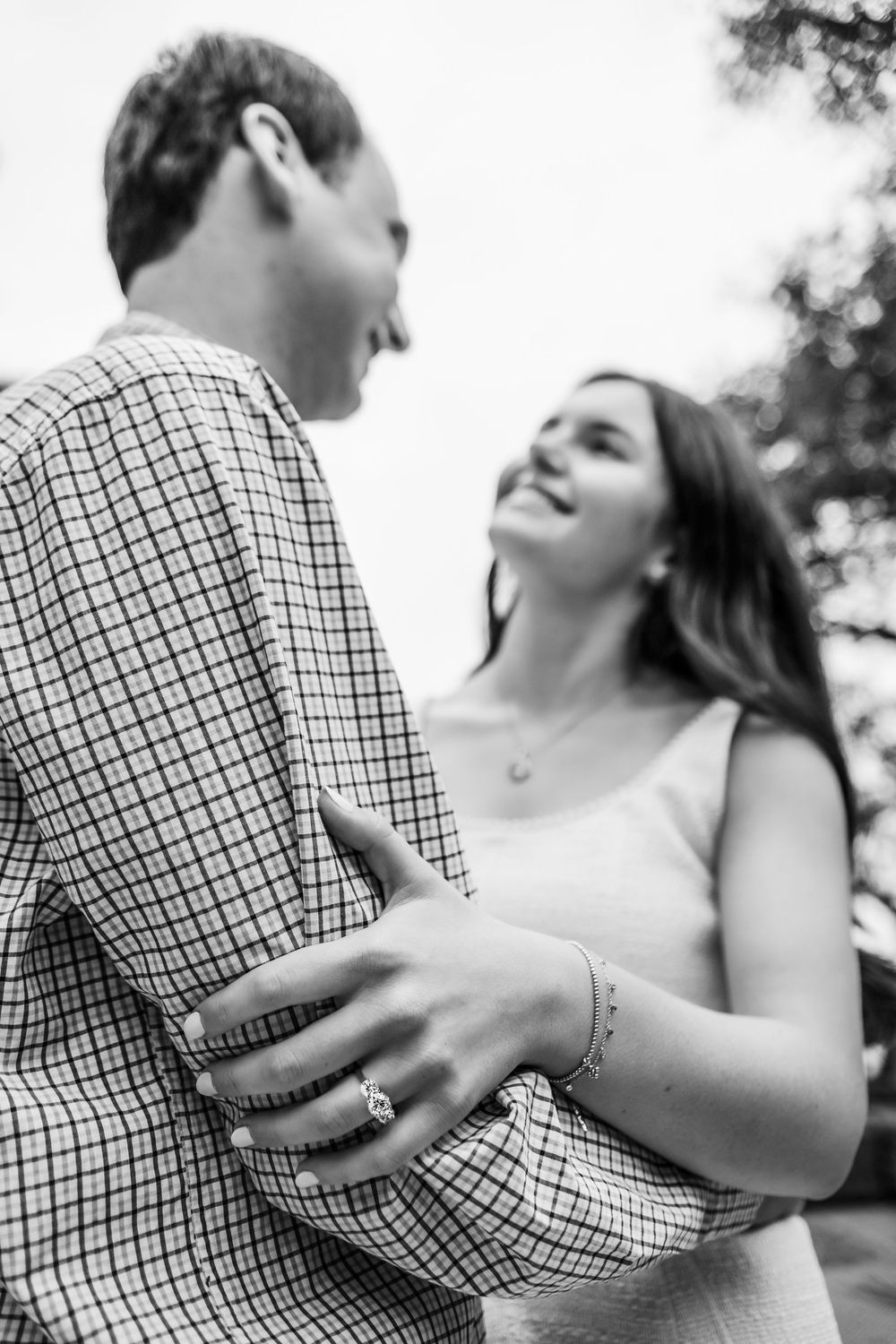 A romantic black and white portrait of a couple embracing and laughing together outdoors.