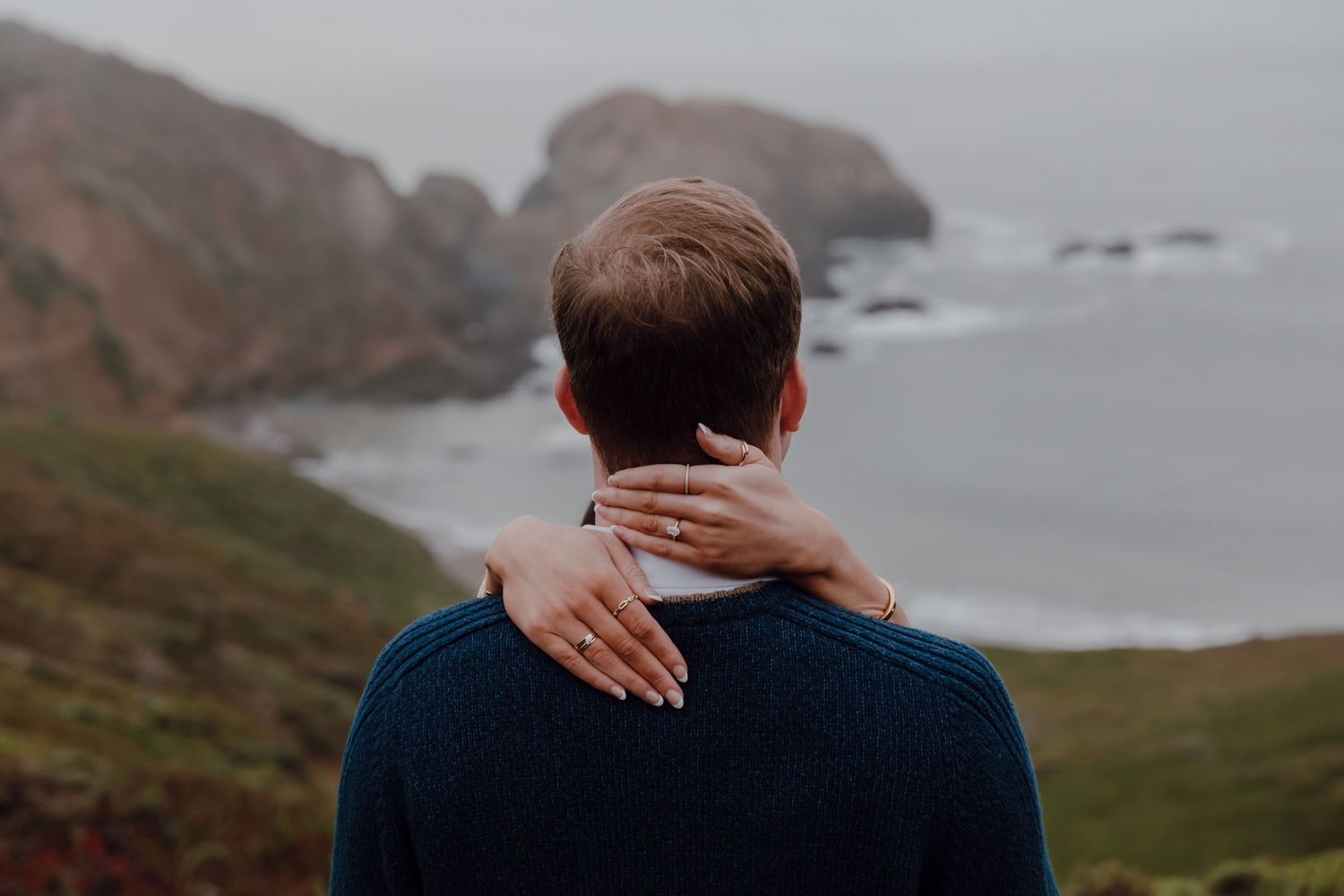 A delicate diamond engagement ring nestled in black velvet surrounded by dried grass and straw in a rustic setting.
