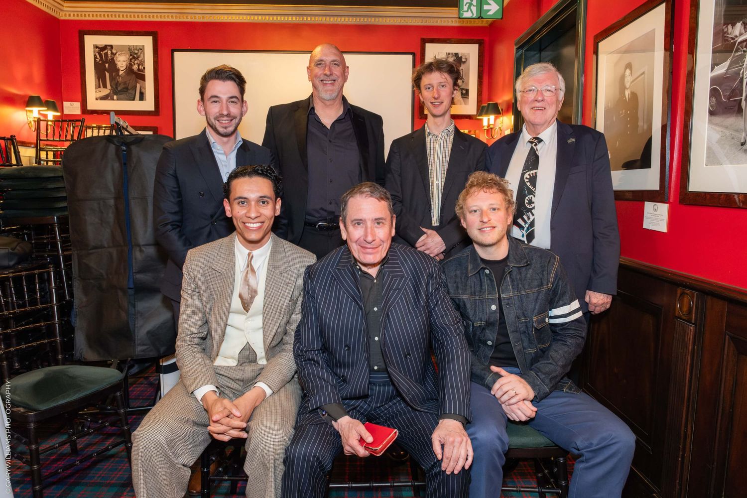 A group of people pose together for a photo in a room with red walls and dark wood paneling.