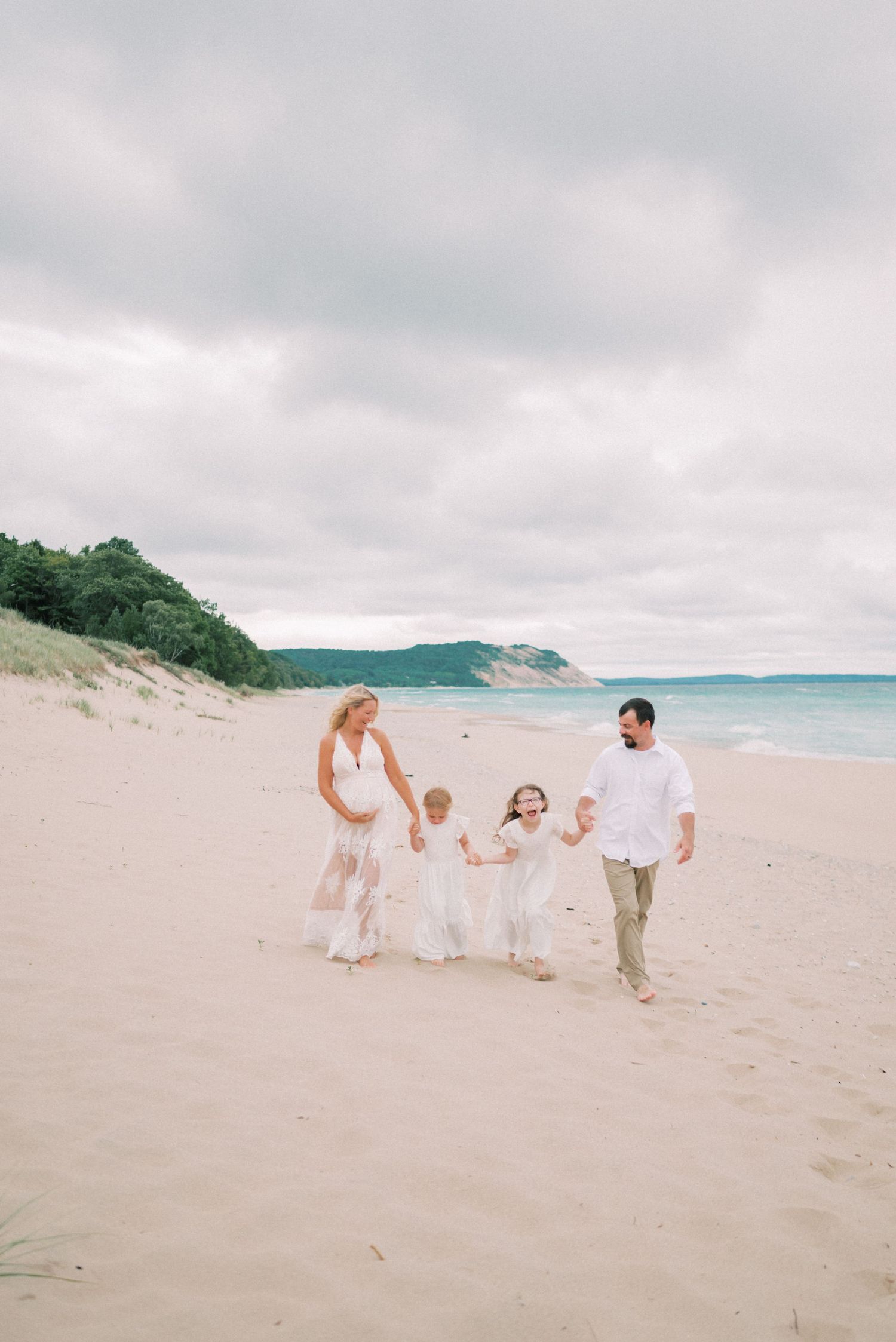 Family of five walking together on a sandy beach with coastal cliffs in background.