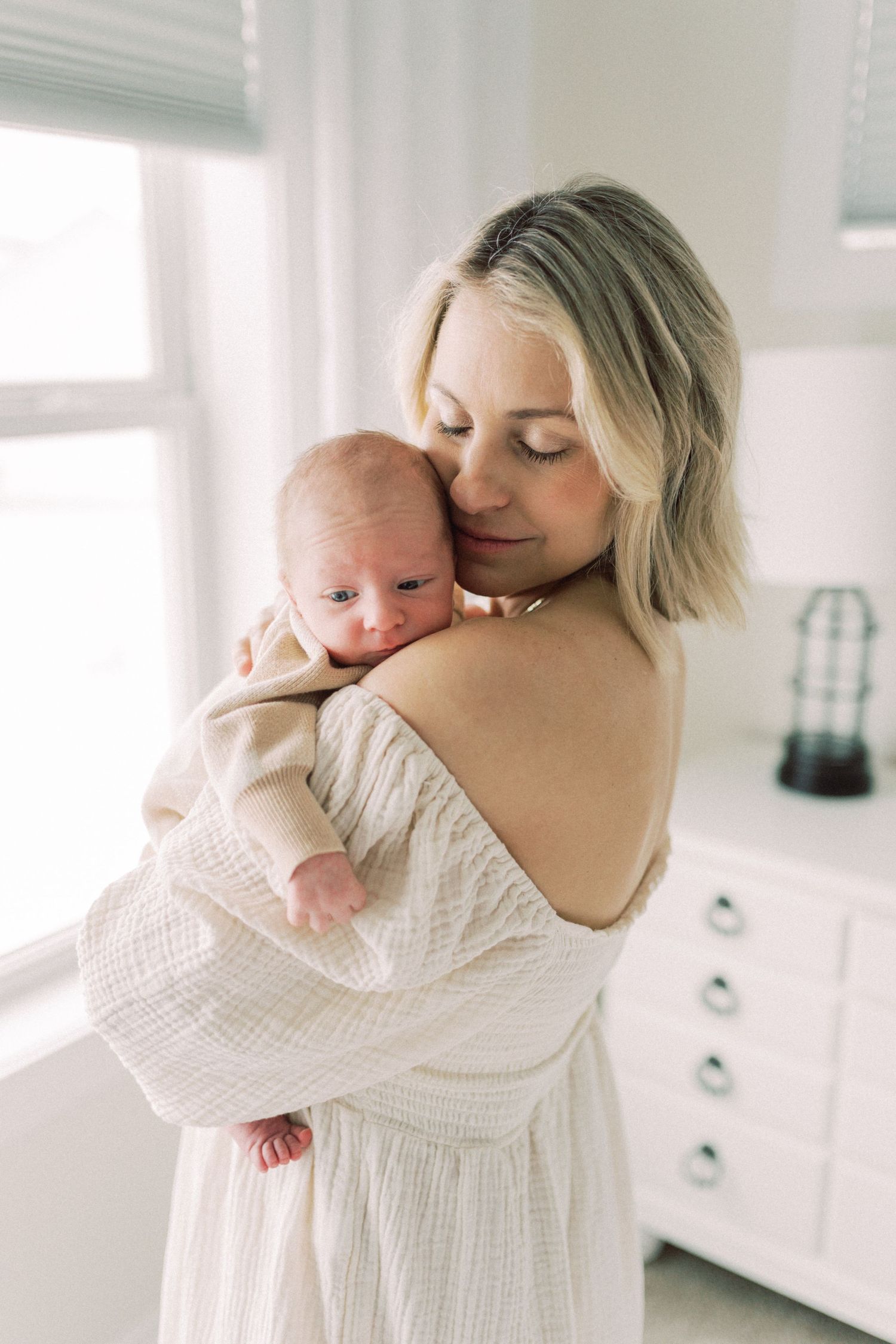 An intimate indoor portrait showing tender care for a baby in soft white surroundings.
