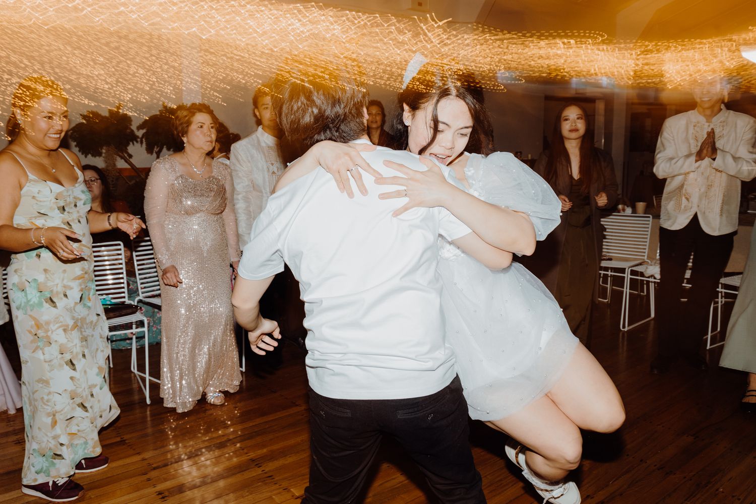 Energetic dancing at a wedding reception with guests in formal attire on a wooden dance floor.