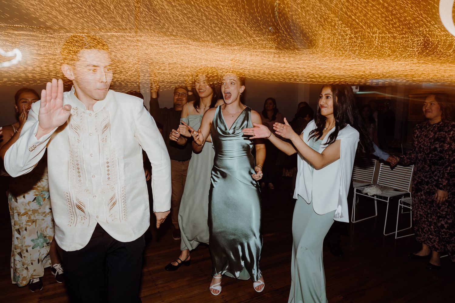 Party guests dancing enthusiastically under decorative ceiling lights at an indoor venue.