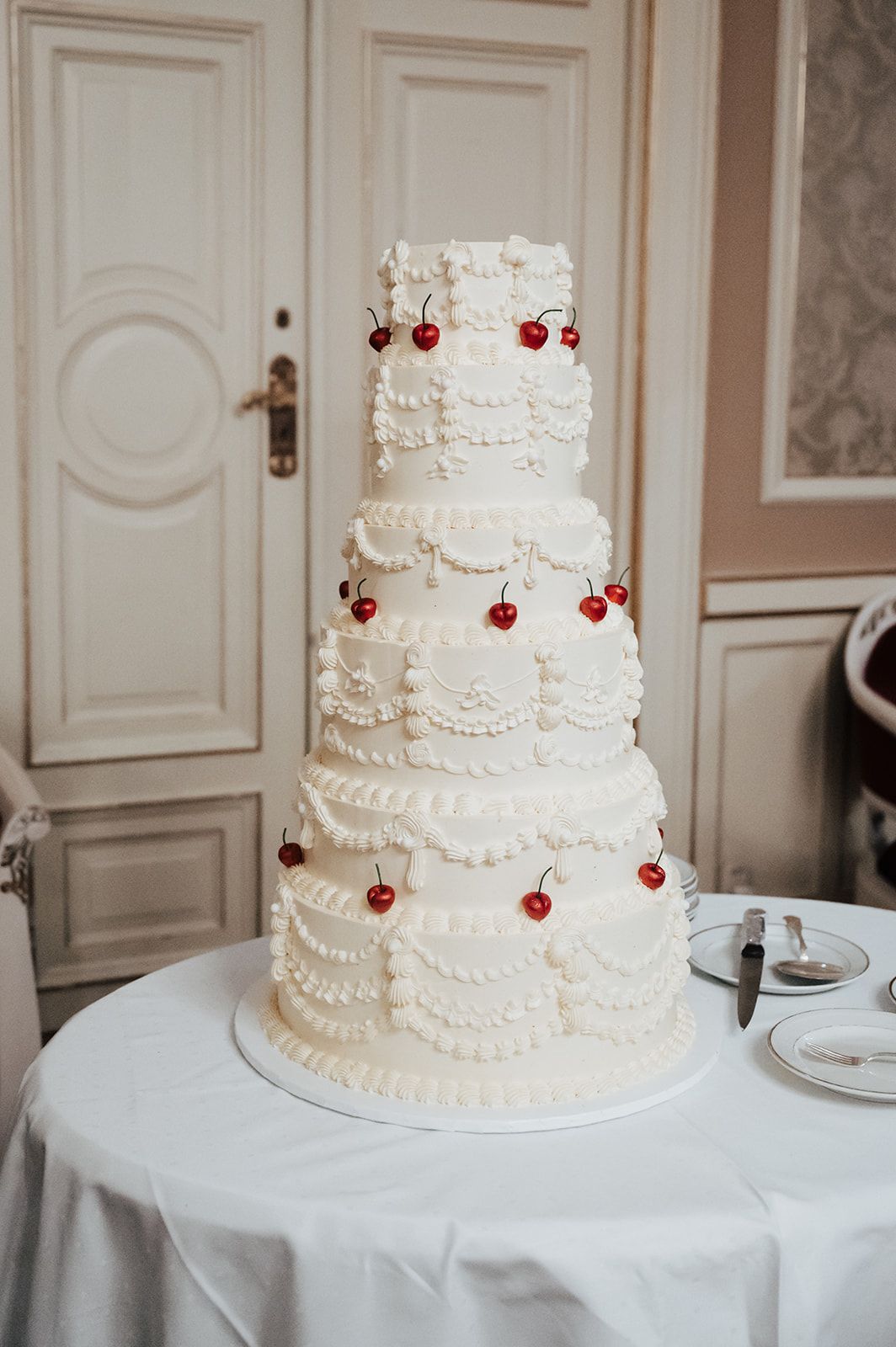 Elegant white tiered wedding cake decorated with delicate lace patterns and small red berries.