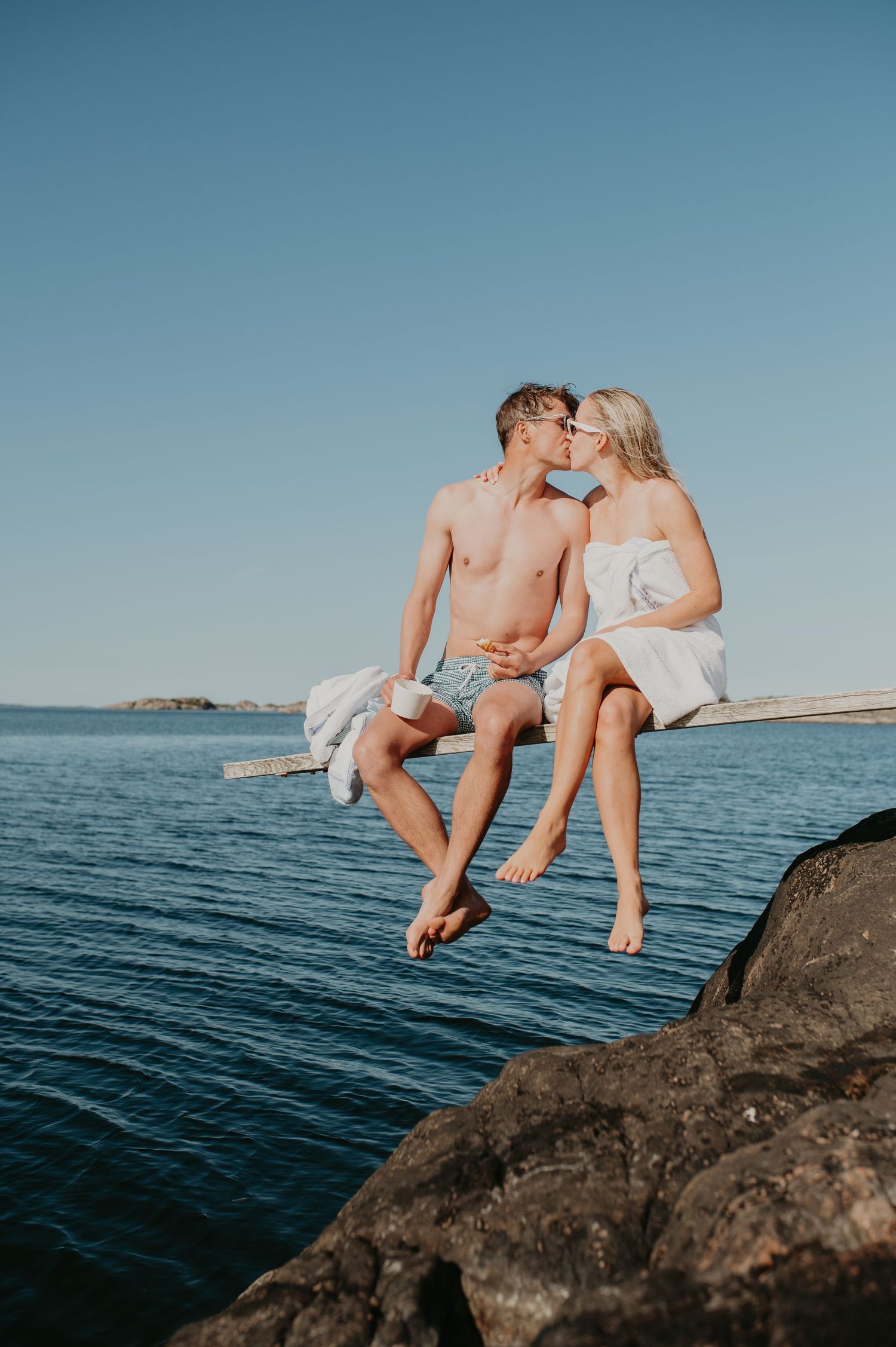 A romantic summer moment of a couple sitting on rocks by a calm blue lake on a sunny day.