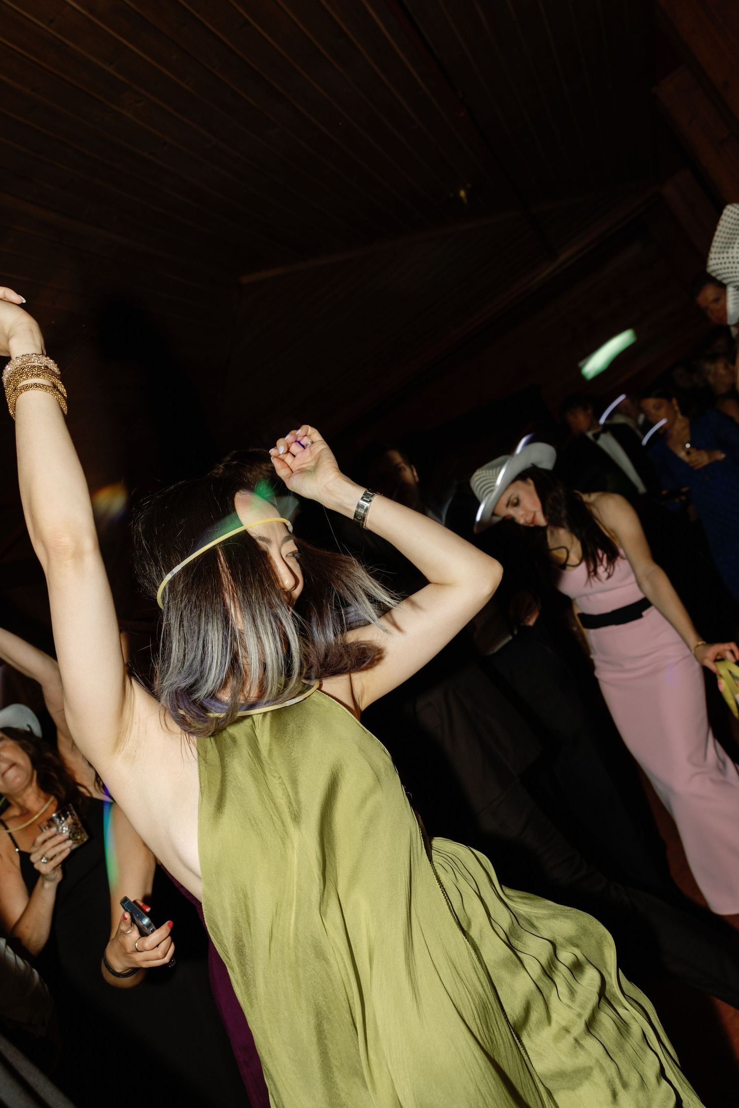 Woman in olive green dress dancing with raised arms at dark indoor party.