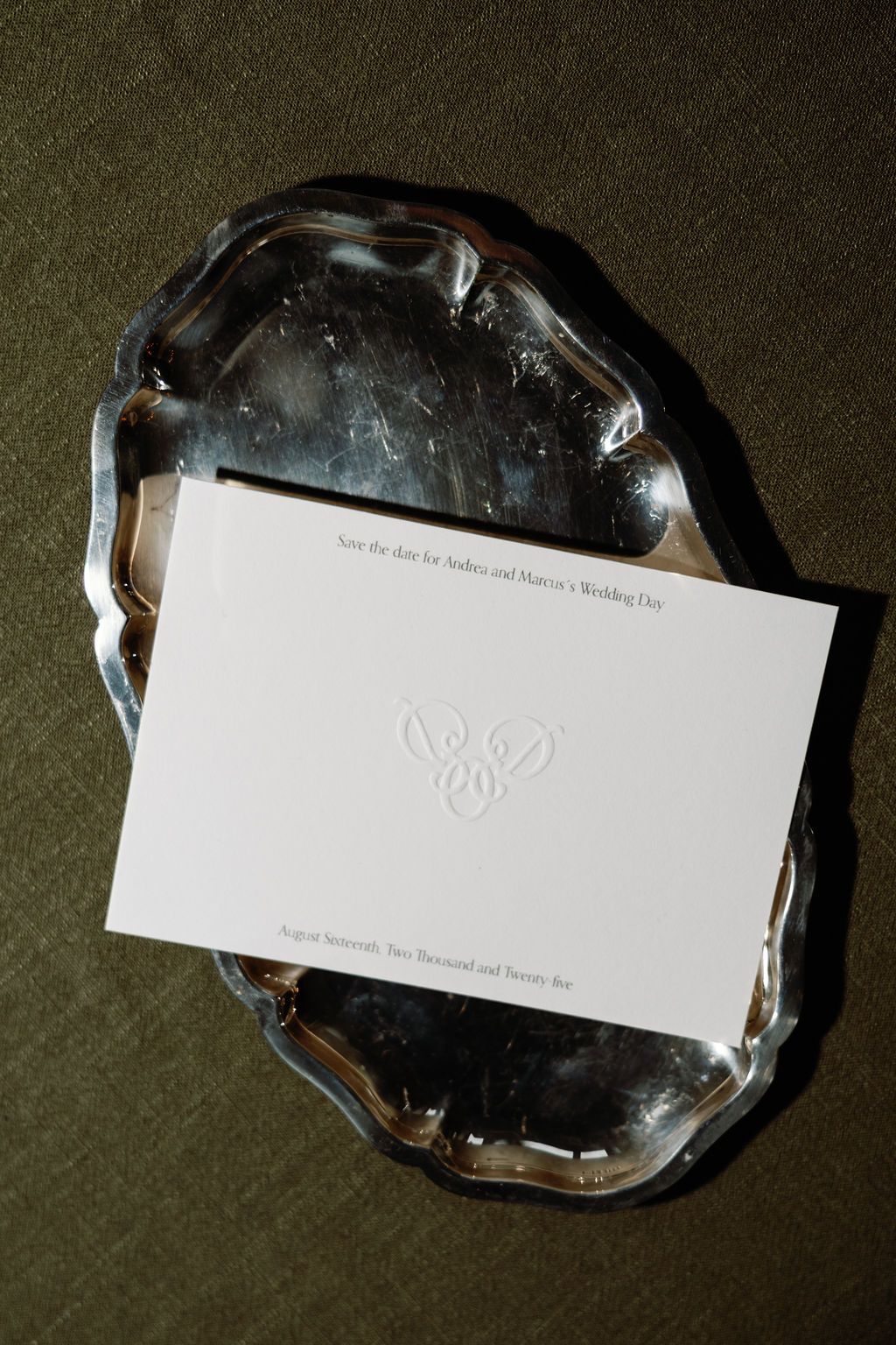 White embossed invitation card displayed on a silver metallic tray.