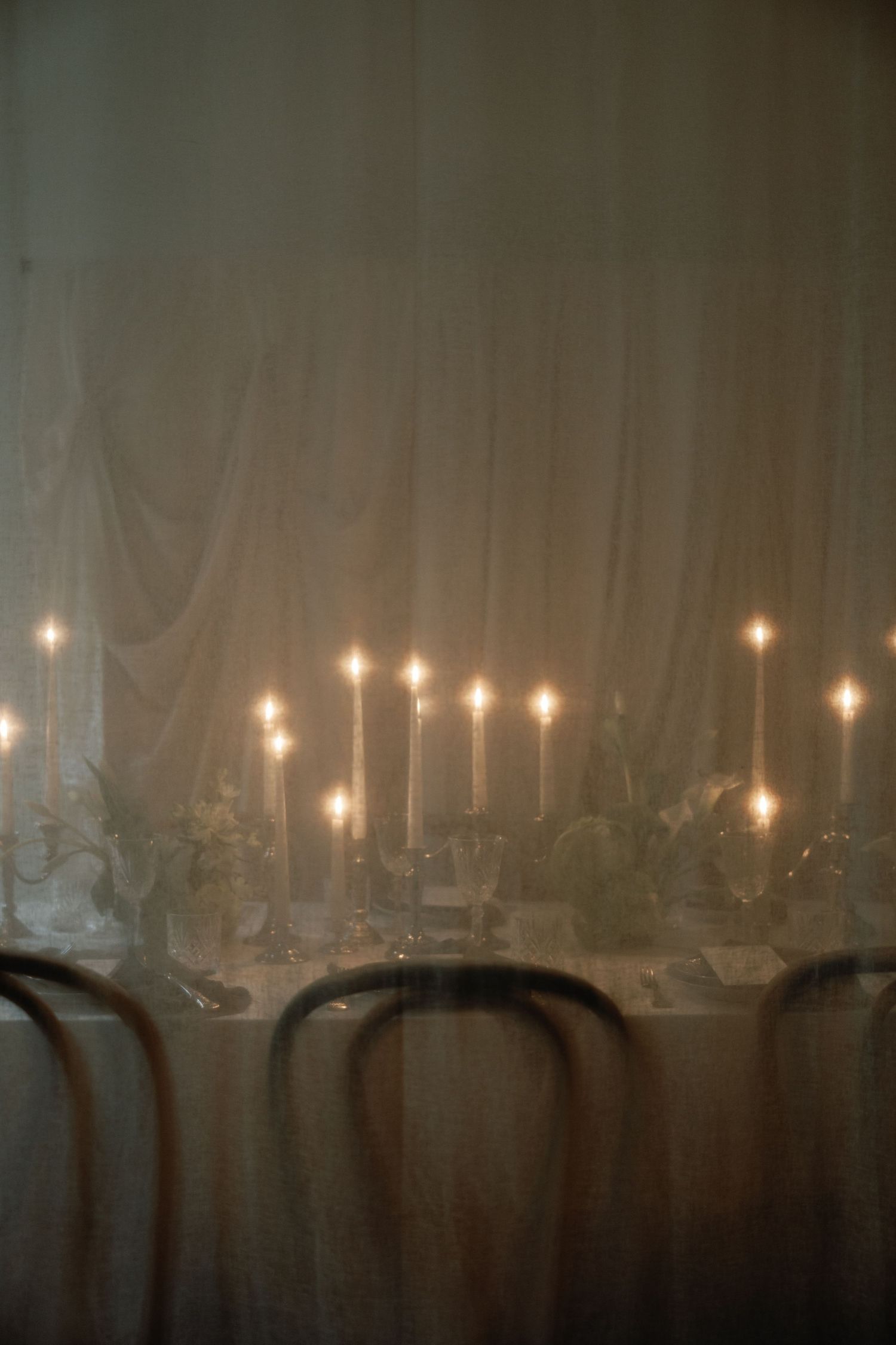 Moody wedding reception table with glowing taper candles against draped fabric.