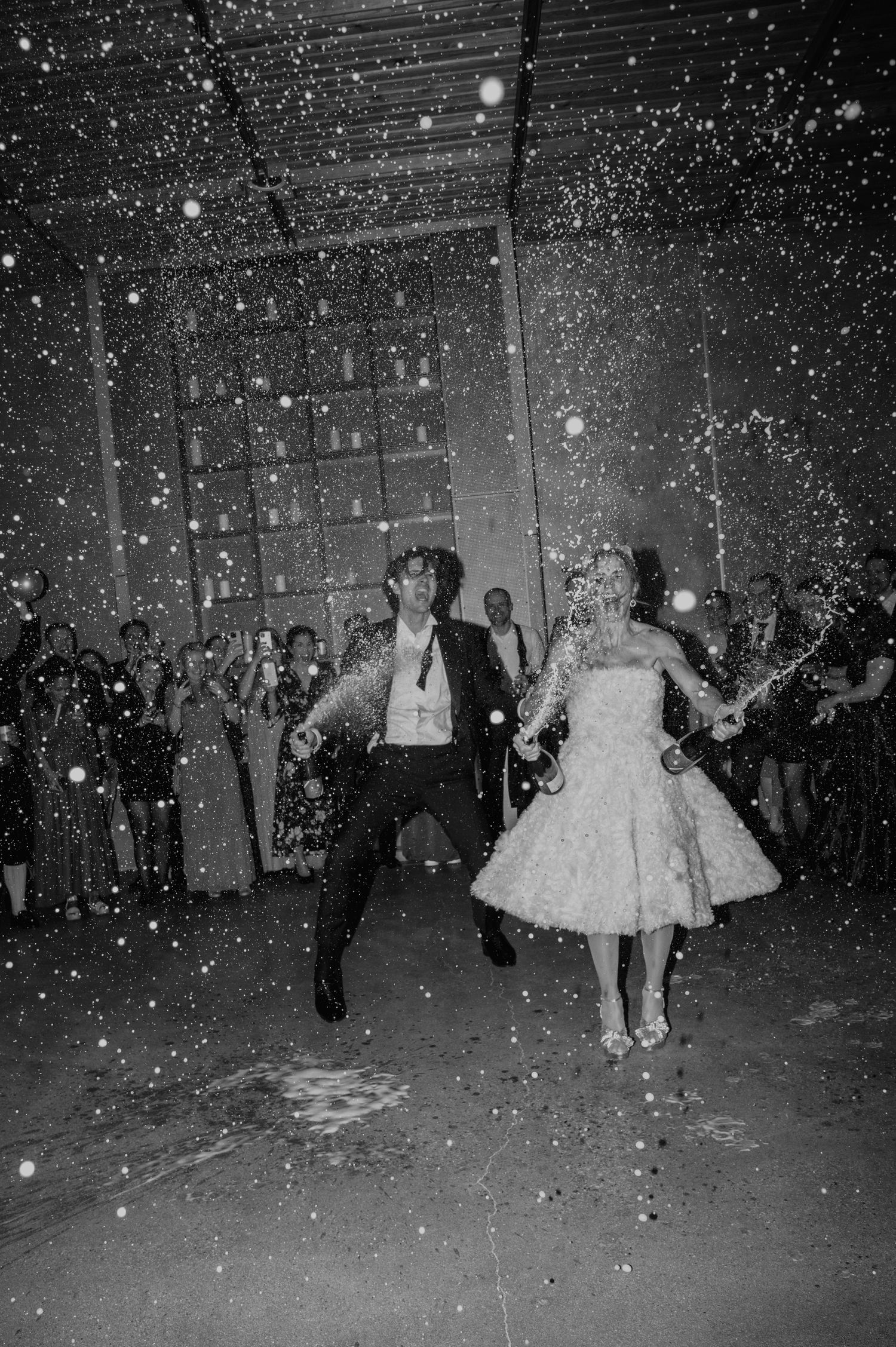 Wedding couple dancing joyfully under falling confetti in black and white.
