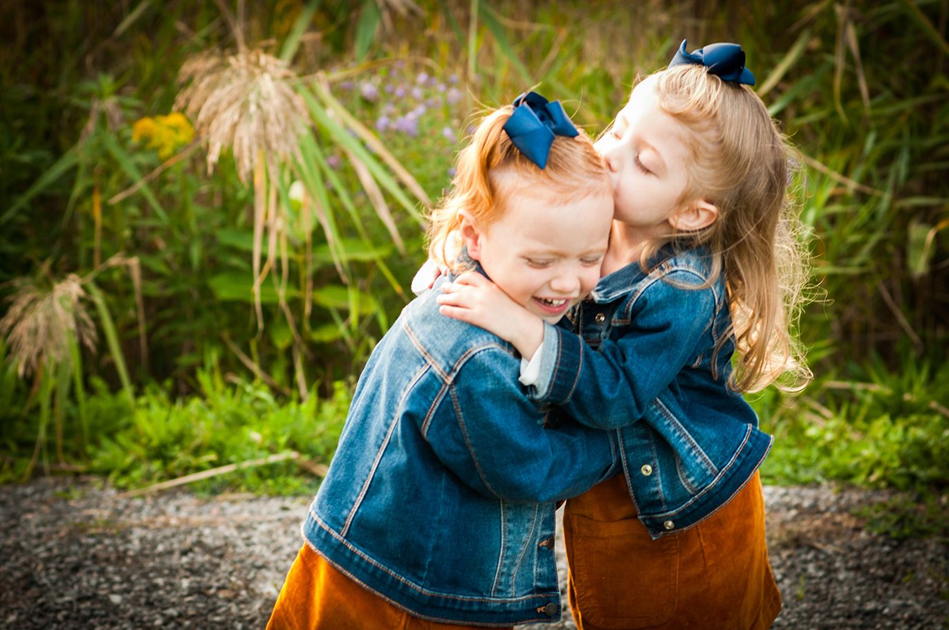 Two young children in denim jackets share a sweet moment together outdoors.