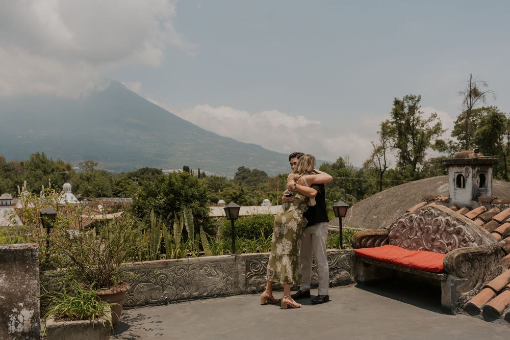 A couple embraces on a rooftop terrace with a majestic volcano vista and lush tropical landscape in the background.