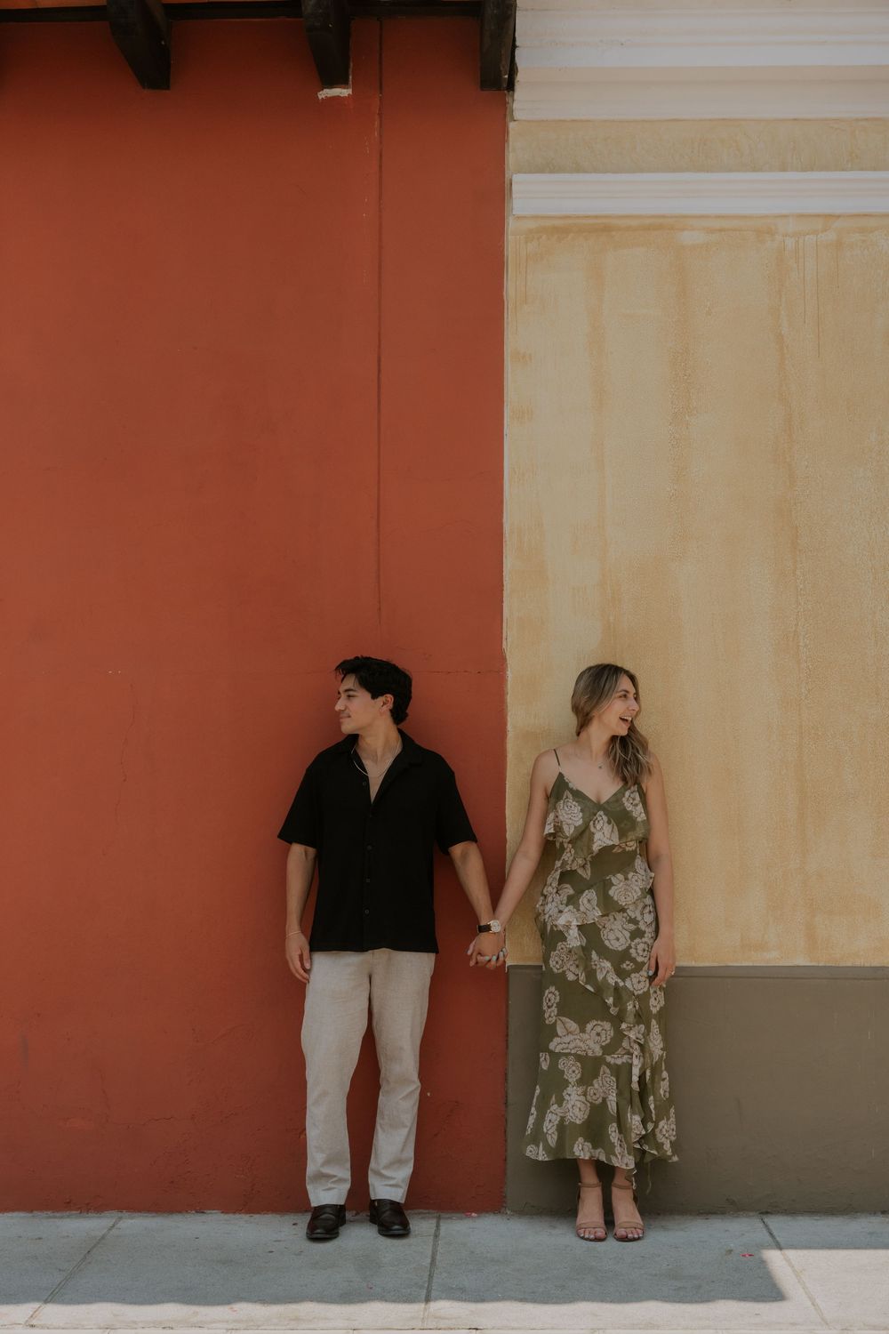 Couple in contrasting outfits posing against coral and cream colored walls in an artistic photo.