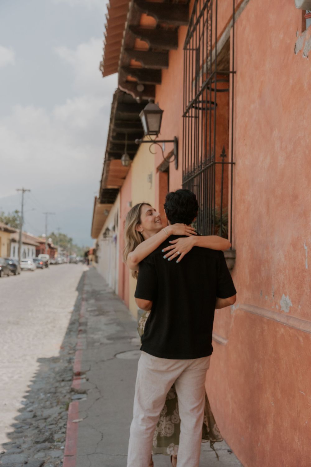 Romantic embrace against a rustic pink wall with traditional lanterns and colonial architecture.
