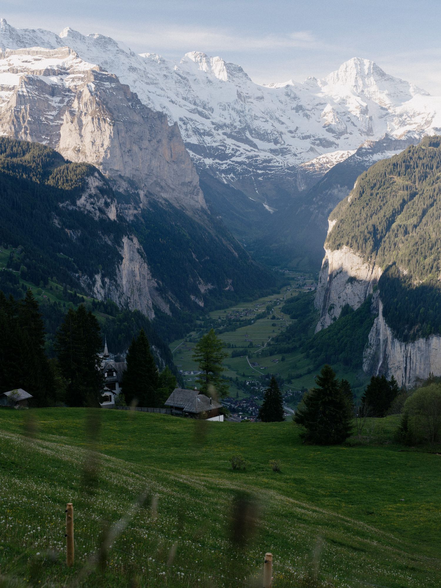 Snow-capped mountains tower over a lush green valley with scattered chalets in the Swiss Alps near Lauterbrunnen.