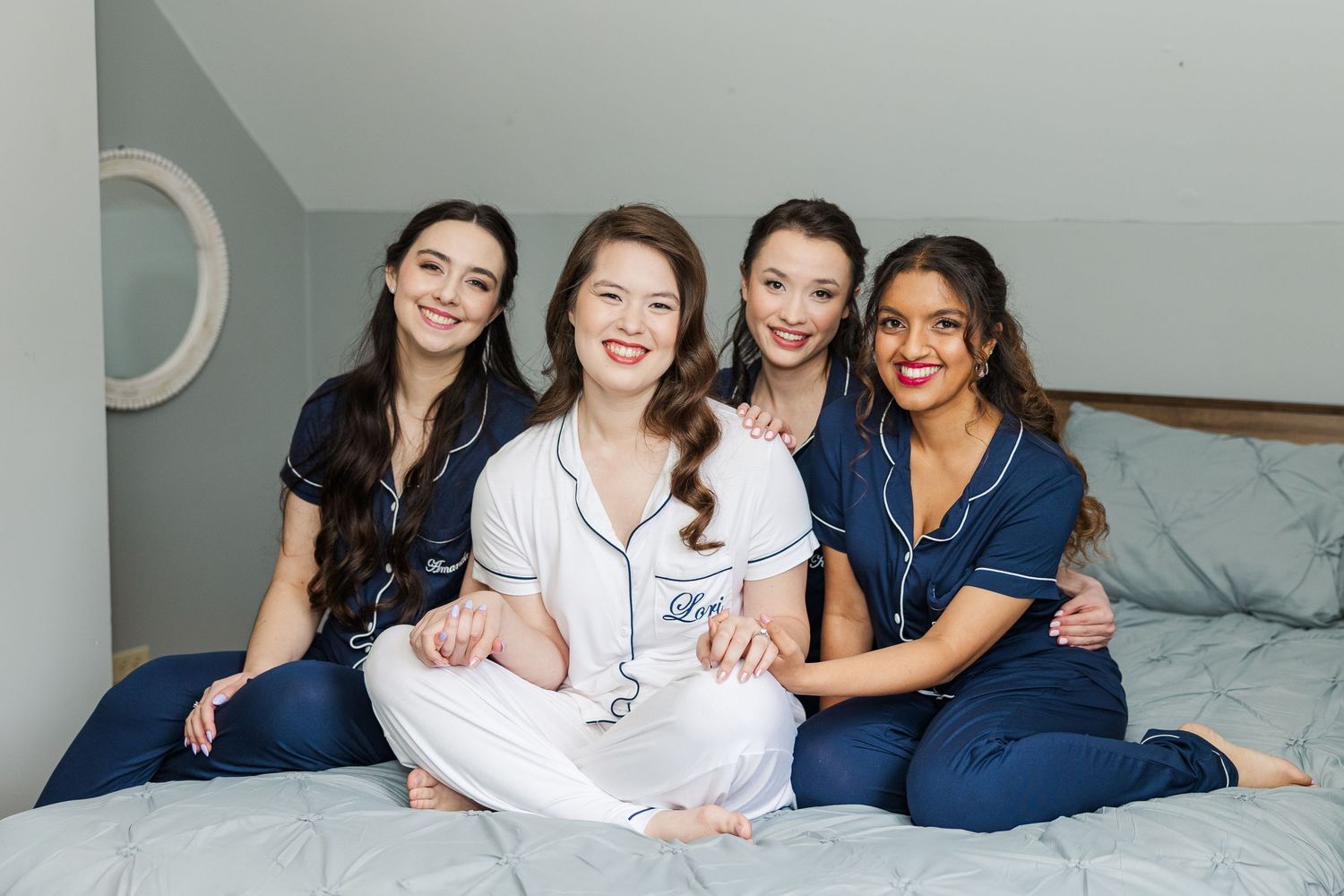 Healthcare workers in blue scrubs sit together on a bed with a patient in white pajamas.