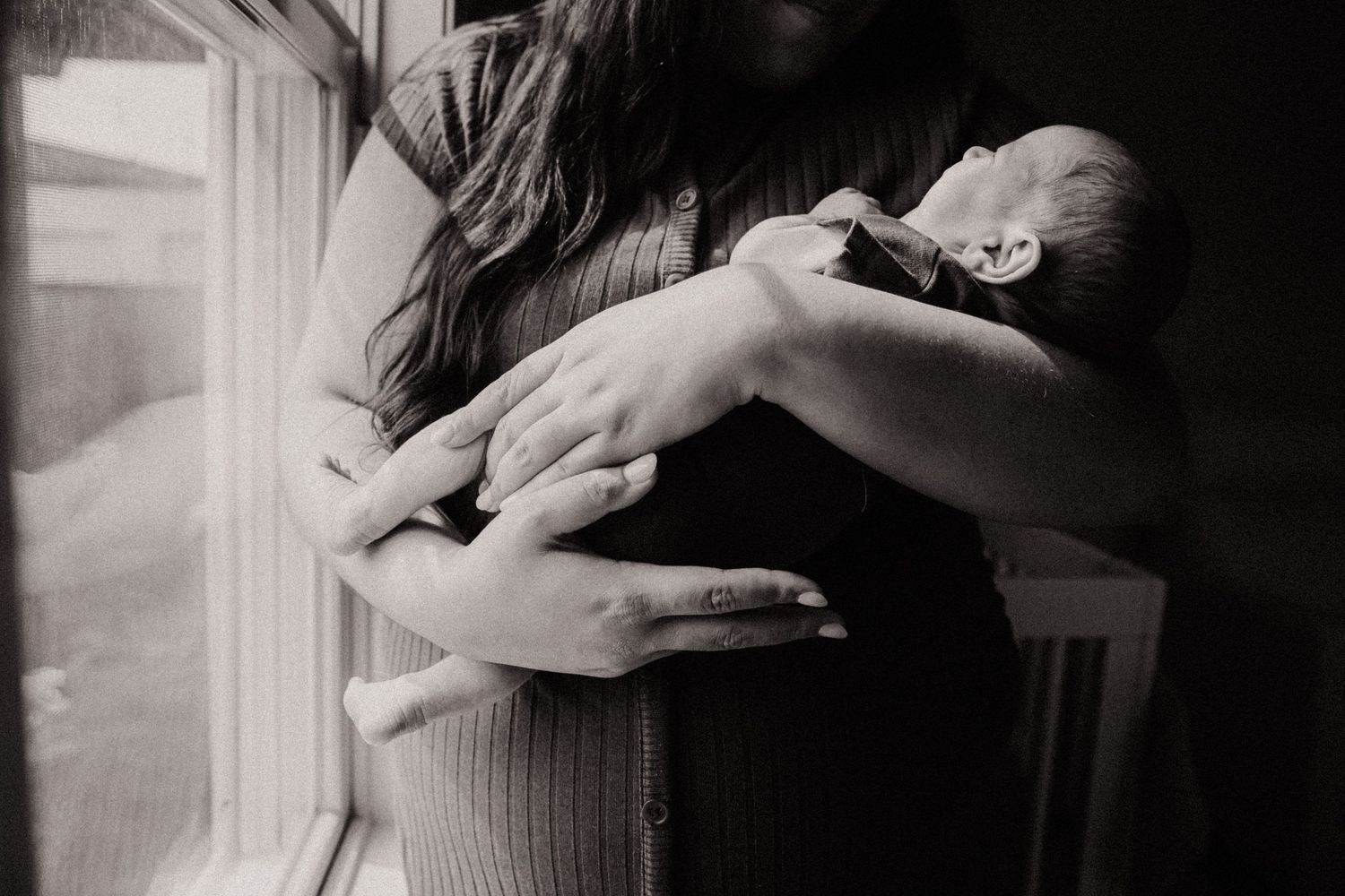 A tender black and white photograph showing a peaceful sleeping baby cradled against someone's chest near a window.