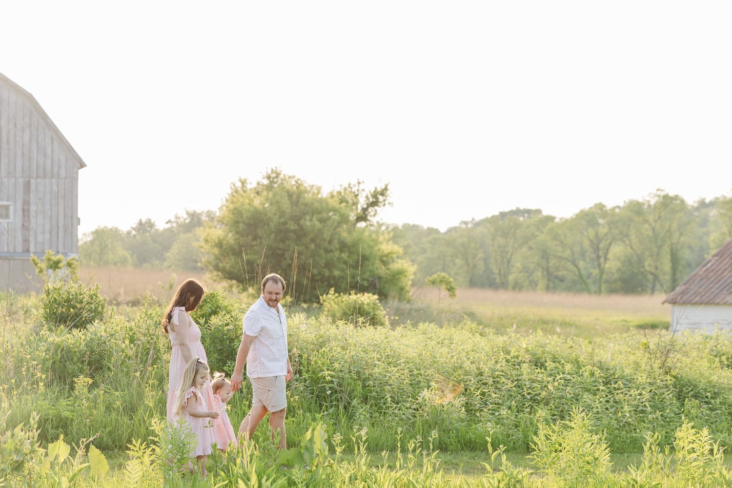 A family stands together in a sunlit meadow with wildflowers and trees during golden hour.
