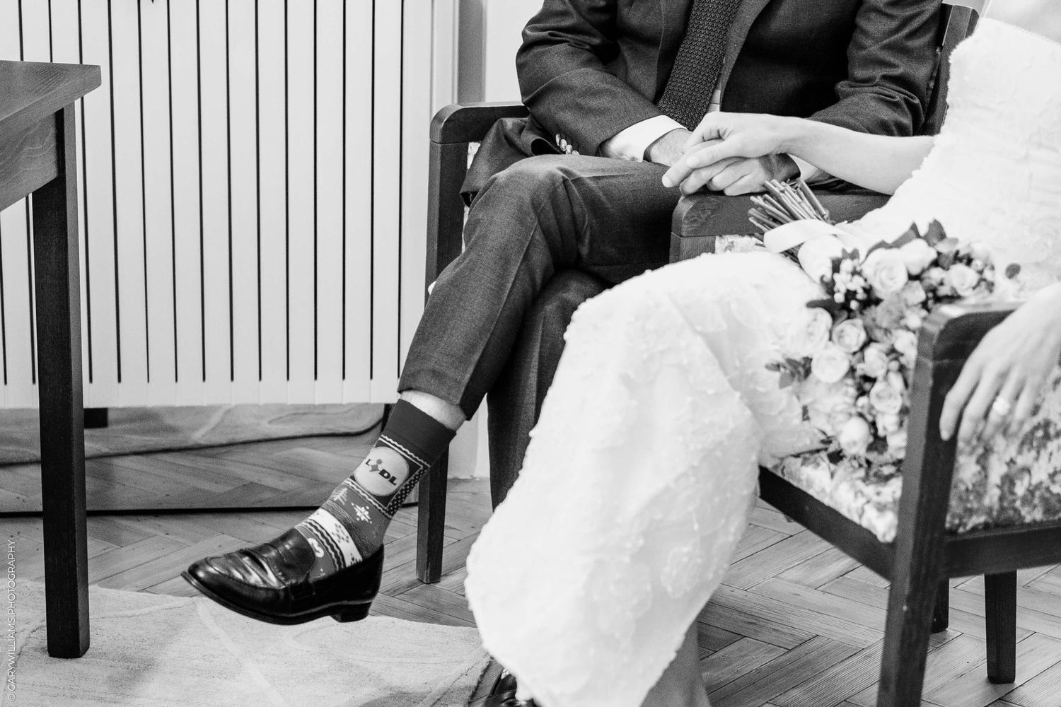 Black and white photo showing crossed legs in dress shoes and socks on an upholstered chair.