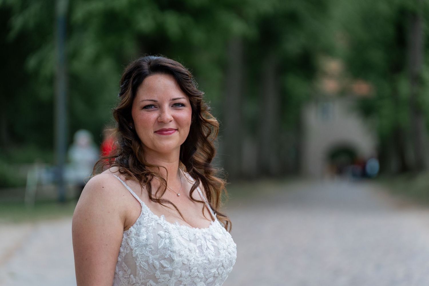 Braut im weißen Kleid lächelt in die Kamera, Bäume im Hintergrund, Schloss Mirow