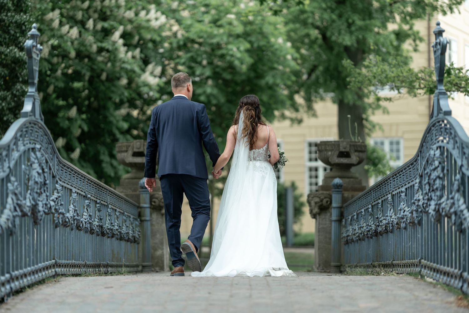 Brautpaar läuft über kleine Eisenbrücke im Park von Schloss Mirow
