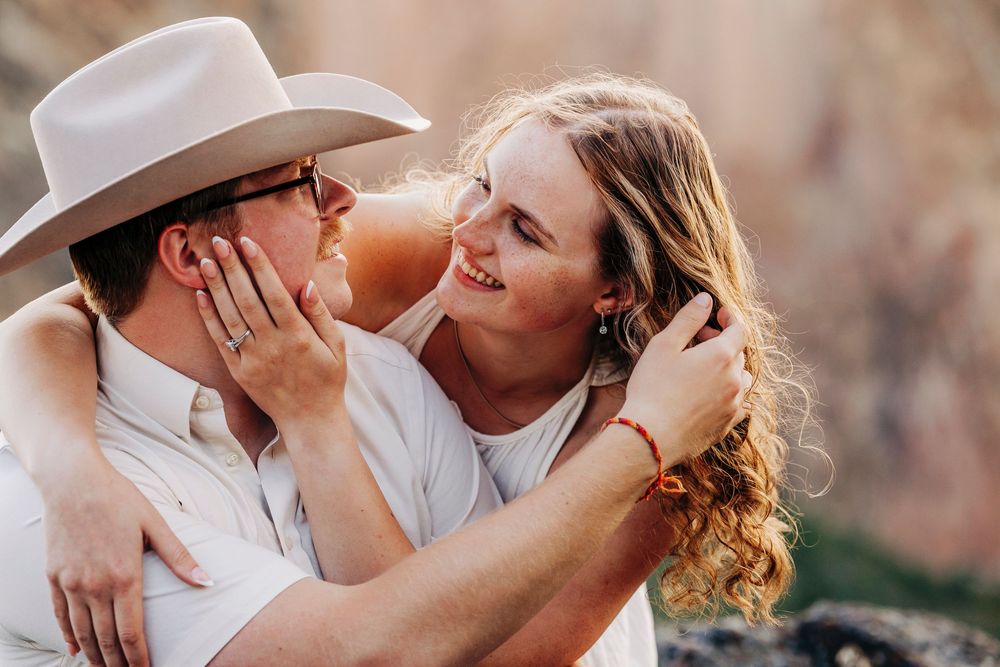 A romantic couple shares an intimate moment outdoors with the person in a cowboy hat.