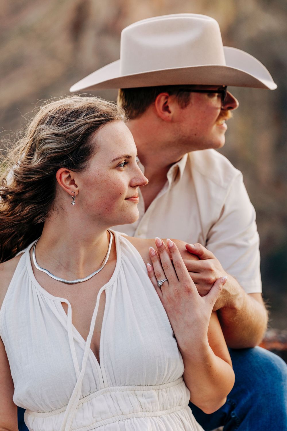 A romantic sunset portrait of a couple embracing outdoors, with one wearing a cowboy hat and white shirt.