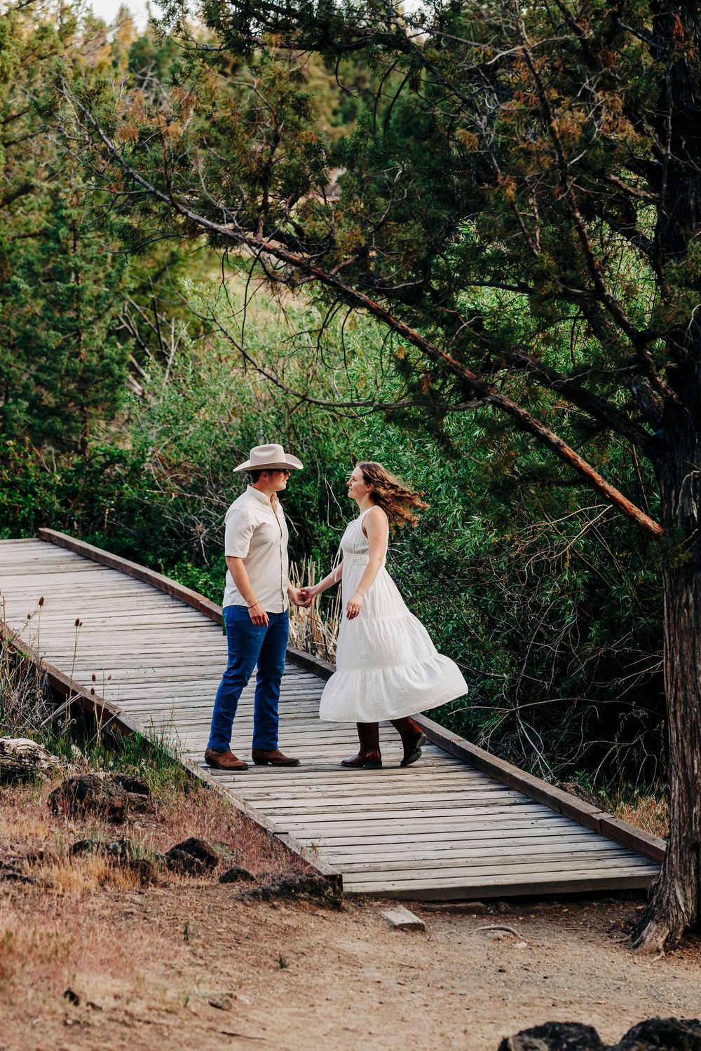 A couple walks along a wooden boardwalk path through a forest setting.