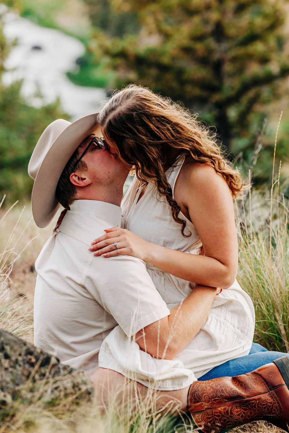 A romantic couple embraces in tall grass at sunset with cowboy boots visible in a rustic outdoor setting.