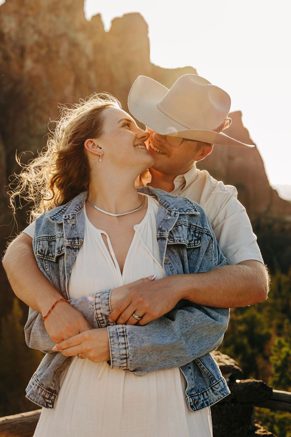 A couple shares an intimate moment at sunset, wearing casual western attire with a denim jacket.